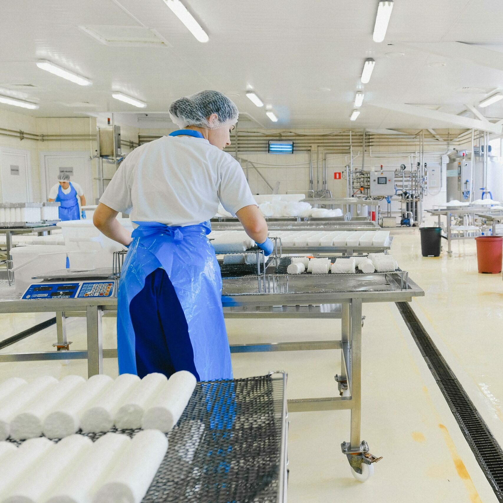 A worker in protective gear handles cheese in a modern dairy factory setting.