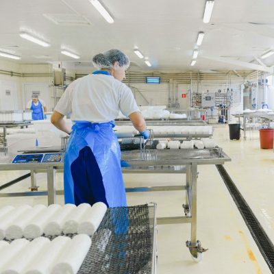 A worker in protective gear handles cheese in a modern dairy factory setting.